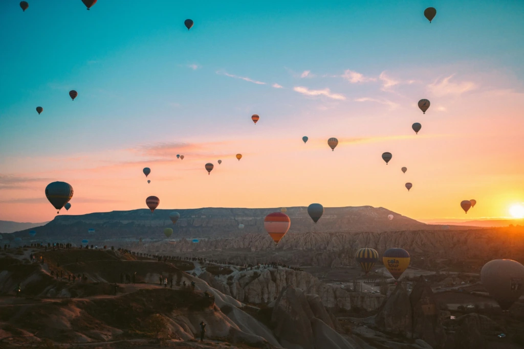 Kapadokya’da gün doğumunda gökyüzünde süzülen sıcak hava balonları ve vadiler üzerinde oluşan romantik manzara.