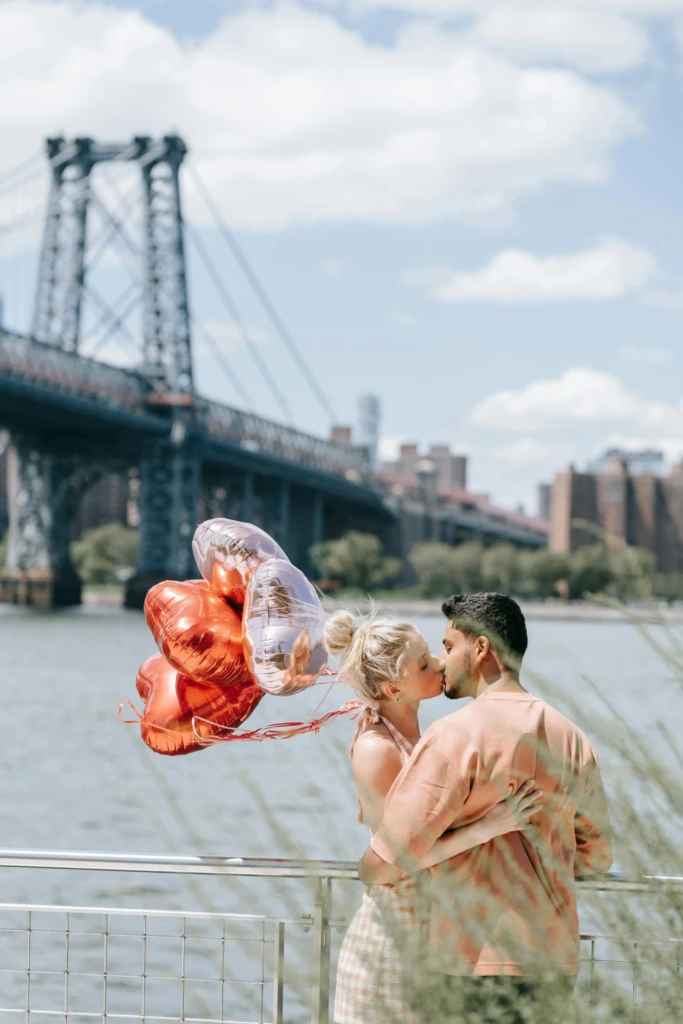 New York Williamsburg Köprüsü önünde kalpli balonlarla romantik bir an paylaşan çift.
