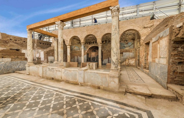 Efes Antik Kent rehberimizle zamanda yolculuk yaptığımız Yamaç Evler'den birinin, karmaşık desenli mozaik zeminleri, zarif sütunları, kemerli duvar resimleriyle süslü odalarını ve lüks yaşam tarzını yansıtan kalıntılarını, modern bir koruma çatısı ve ziyaretçi platformu altında gösteren etkileyici bir görüntü.