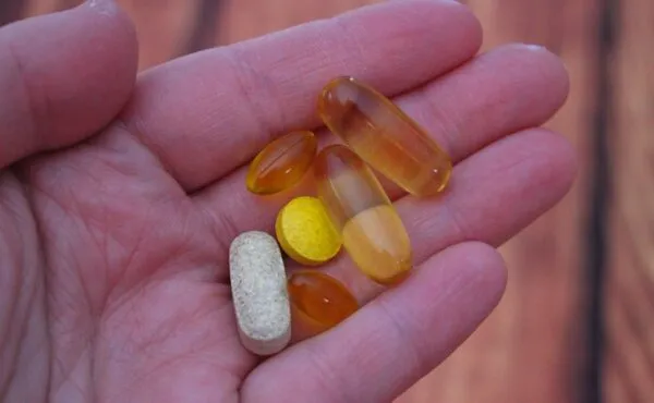 Bir elde tutulan çeşitli vitamin ve takviye hapları; vegan beslenmede eksikliği olabilecek B12, D vitamini ve omega-3 desteği için.