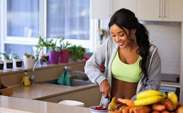 Mutfakta meyve hazırlayan, spor kıyafetli genç bir kadın; sağlıklı ve mutlu vegan yaşam tarzını yansıtıyor.