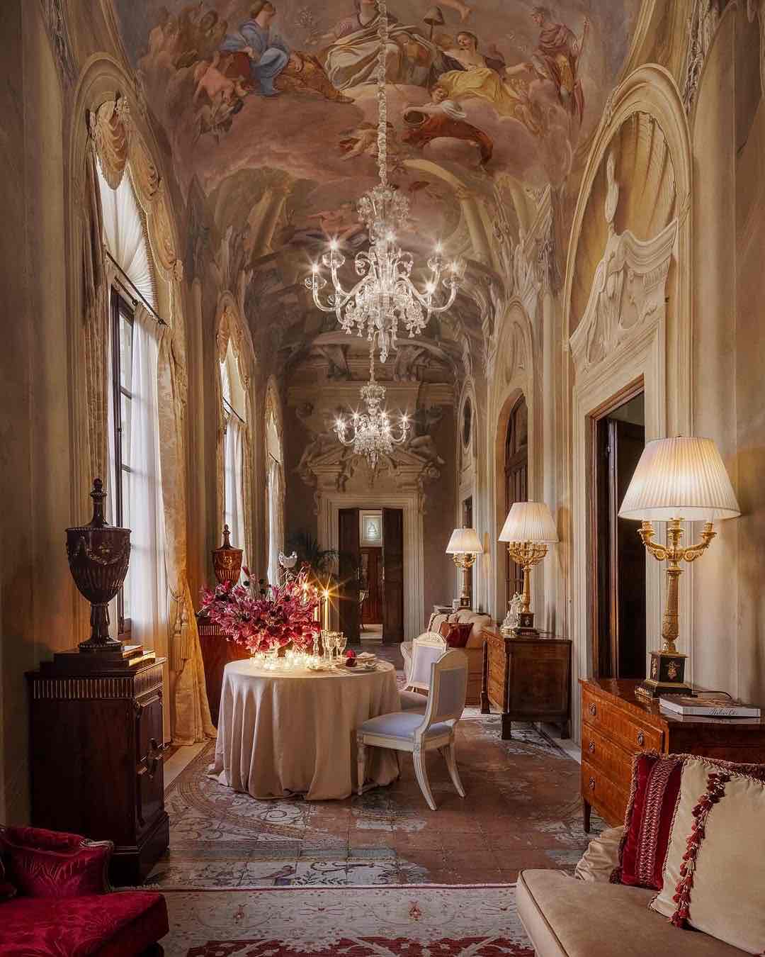 Four Seasons Oteli'nin fresklerle süslü tavanlı, tarihi koridorunda iki kişilik romantik bir akşam yemeği masası. Kristal avizeler ve mum ışığı lüks atmosferi aydınlatıyor.