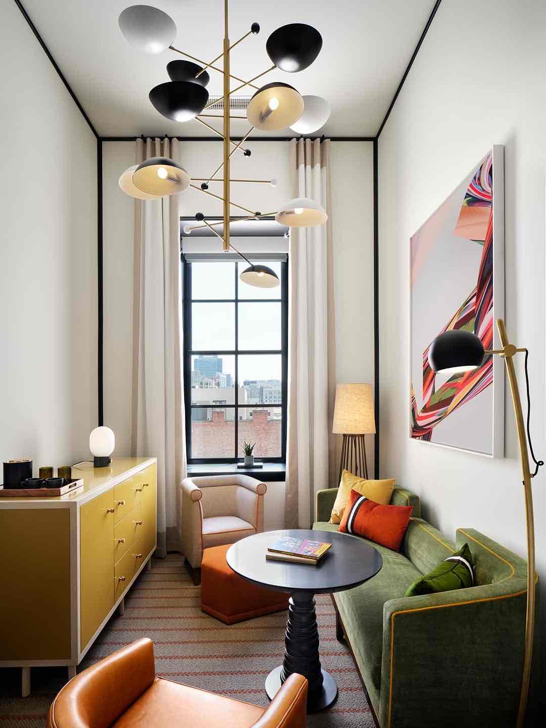 Müze-otel konseptini yansıtan, sanatsal tasarımlı bir oda. Heykelsi avize, yeşil kadife kanepe, sarı konsol ve modern sanat eseriyle odanın eklektik ve şık stili vurgulanıyor.