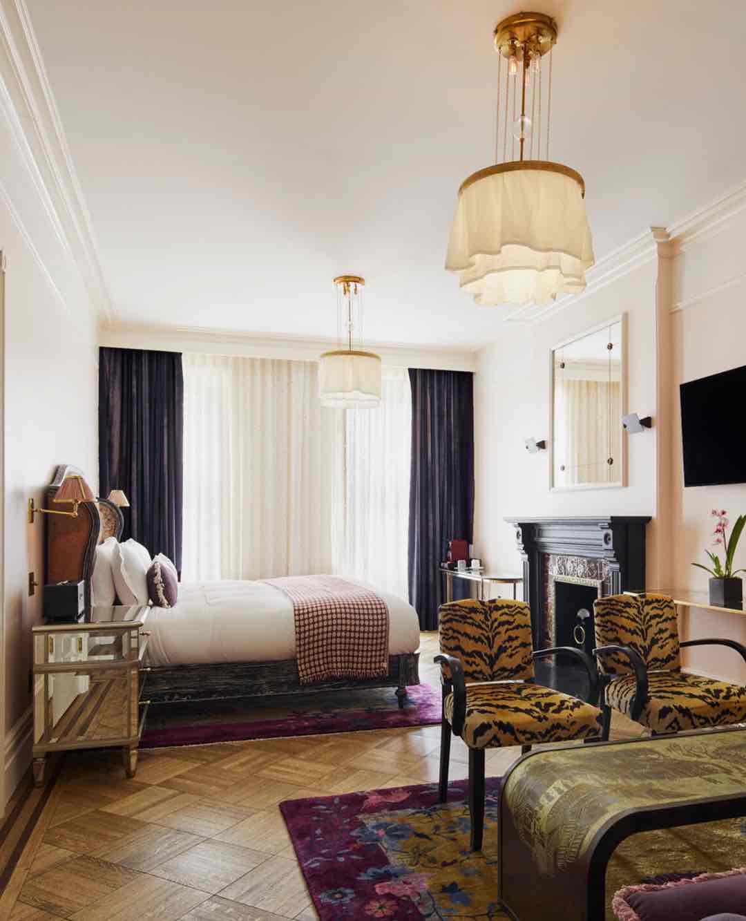 The Hotel Chelsea'nin yenilenen odası, kaplan desenli sandalyeler, klasik şömine ve modern avizelerle bohem ve lüks bir atmosfer yaratıyor. Parke zemin ve zengin dokular tasarımı tamamlıyor.