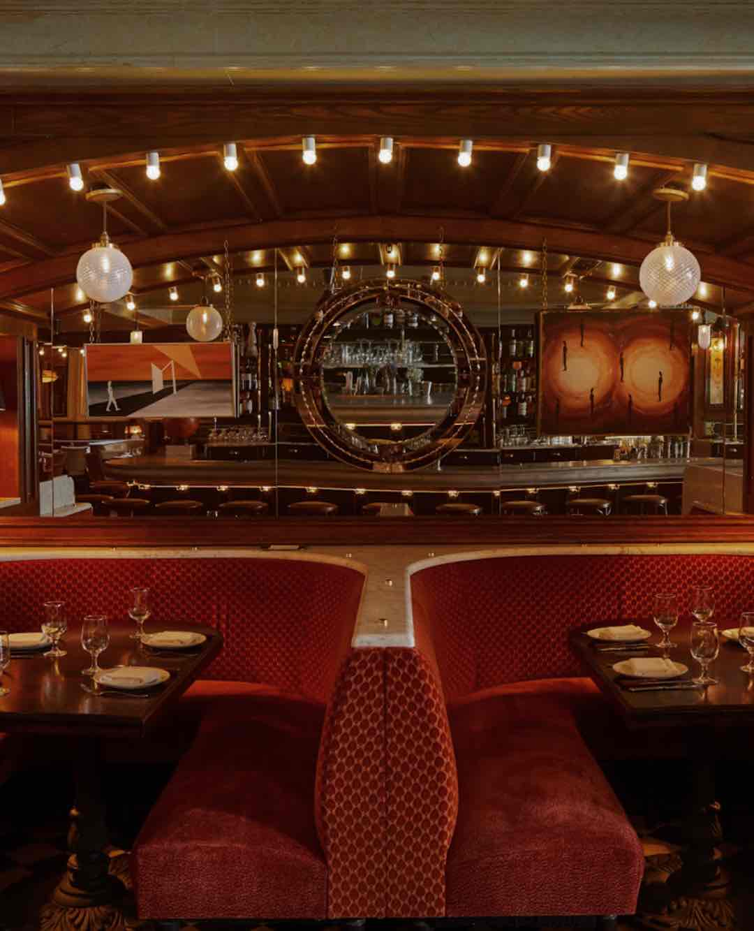 The Hotel Chelsea barının loş iç mekanı. Ön plandaki kapitone kırmızı kadife localar, arkadaki aynalı, ahşap panelli ve sıcak ışıklarla aydınlatılan bar bölümüne bakıyor.