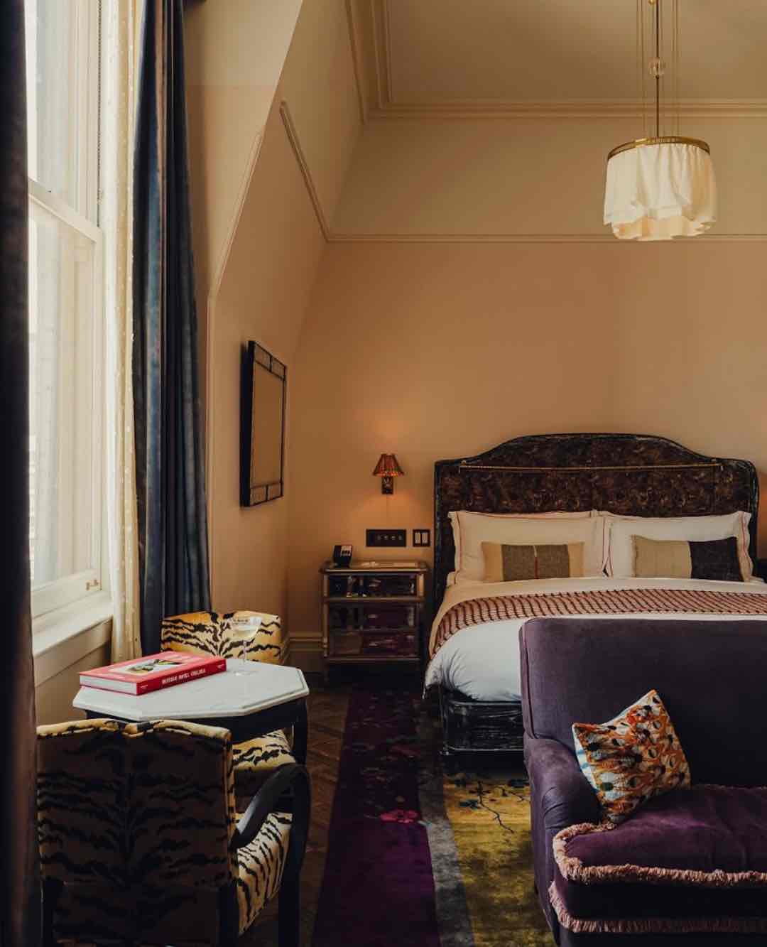 The Hotel Chelsea'deki bir süitin sanatsal ve bohem dekorasyonu; mor kadife bir kanepe, kaplan desenli sandalyeler ve koyu renkli, işlemeli bir yatak başlığı otelin özgün ruhunu sergiliyor.
