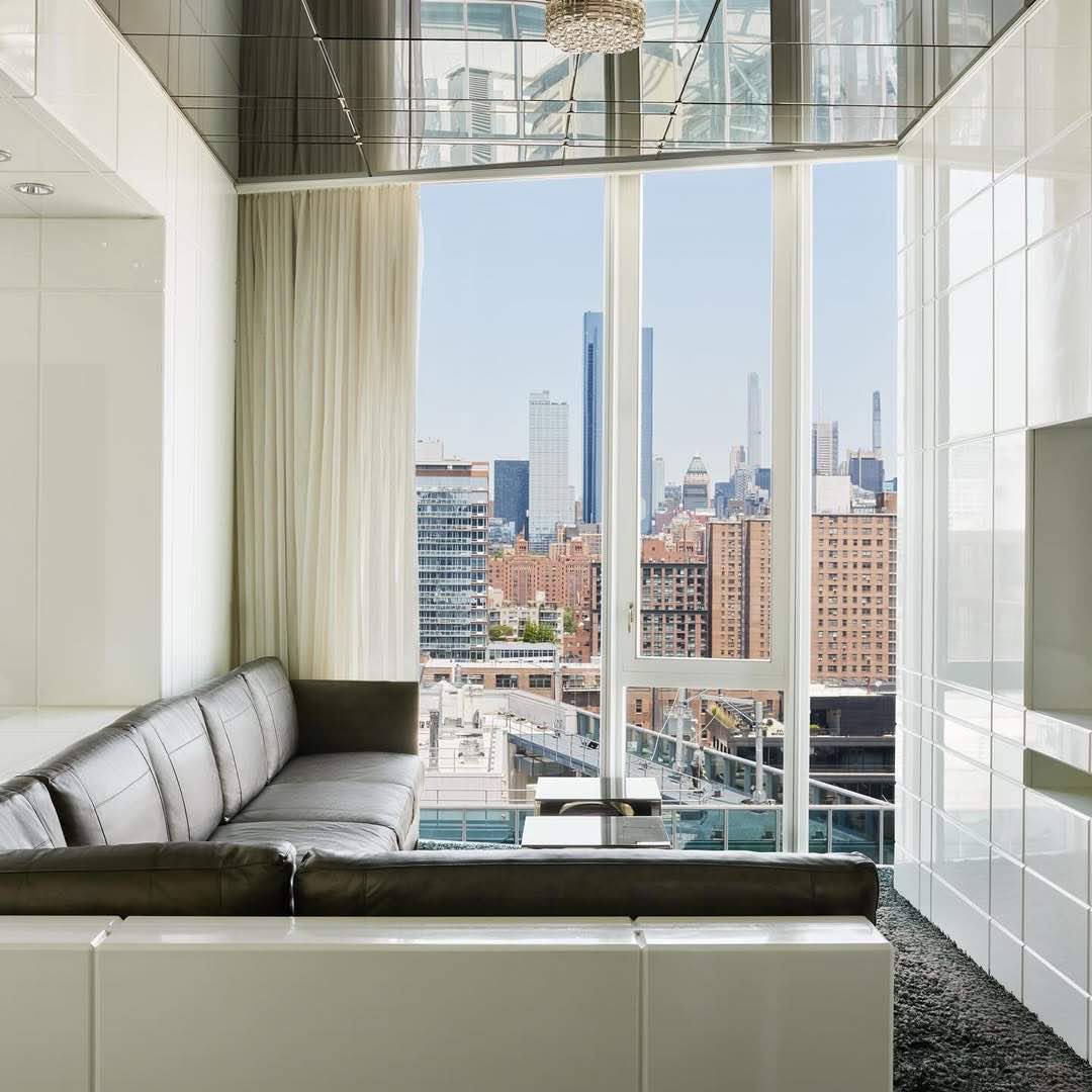 The Standard otelinin modern süitinde, koyu renk deri kanepe, yerden tavana uzanan pencerelerden görünen panoramik New York şehir manzarasına bakıyor. Yansımalı tavan odaya derinlik katıyor.