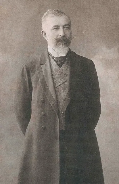 Türk edebiyatının realist akımının önde gelen temsilcilerinden Halid Ziya Uşaklıgil'in, bakışları ileri dönük, sakallı ve bıyıklı yüzünü gösteren, resmi takım elbisesiyle ayakta durduğu eski, sepya tonlarında bir portre fotoğrafı.