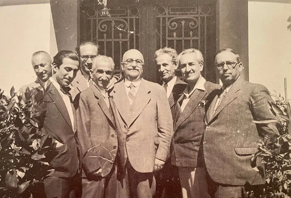İbrahim Çallı ve arkadaşlarının yer aldığı, dış mekanda bir binanın önünde, hepsi koyu renk takım elbiseler giymiş sekiz erkeği gösteren, sepya tonlarında tarihi bir fotoğraf; gruptaki belirgin bıyıklı ve gözlüklü merkez figür İbrahim Çallı'dır.