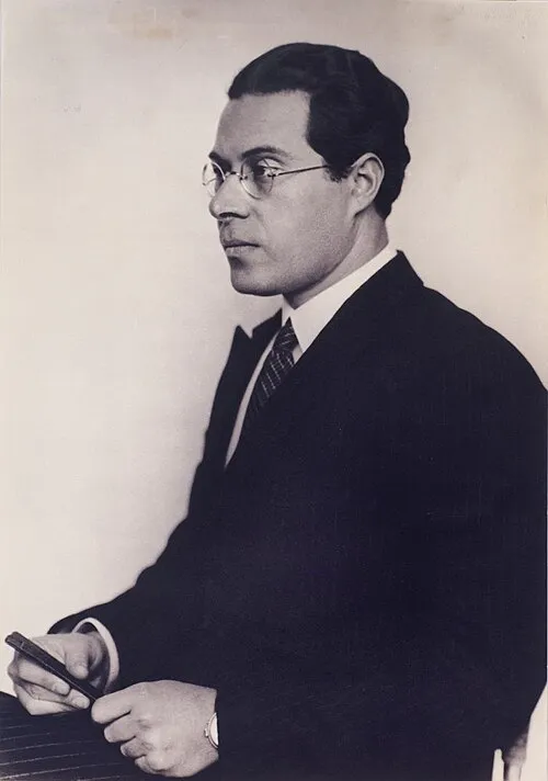 László Moholy-Nagy'nin sağa doğru bakan, yuvarlak gözlüklü, koyu renk takım elbise, beyaz gömlek ve çizgili kravat giyen, elinde dikdörtgen bir nesne tutarken çekilmiş siyah beyaz profil portresi, sanatçının ciddi ve entelektüel duruşunu yansıtıyor.