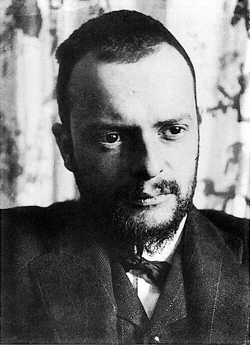 1911 tarihli bu siyah beyaz portrede, hafifçe sola dönük başıyla doğrudan bakışları olan, kısa koyu saçlı ve sakallı genç sanatçı Paul Klee koyu bir ceket ve papyonla poz veriyor, arka plan bulanık ve desenli.