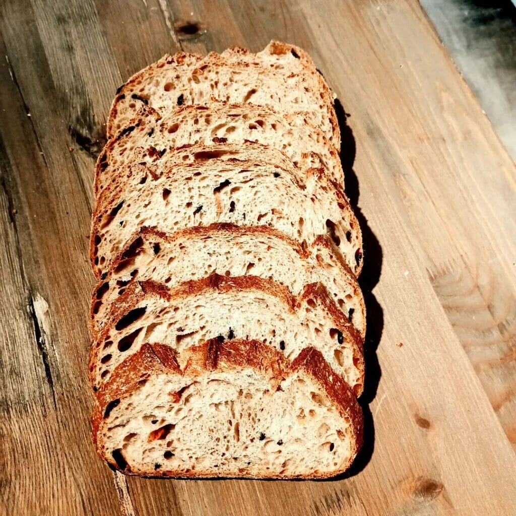 Breadtaking’in el yapımı ekşi mayalı zeytinli ekmeği; ahşap zemin üzerinde dilimlenmiş halde sunulmuş.