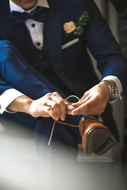 Damat, düğün sabahı lacivert takım elbisesiyle kahverengi ayakkabısını bağlarken şıklığını tamamlıyor.