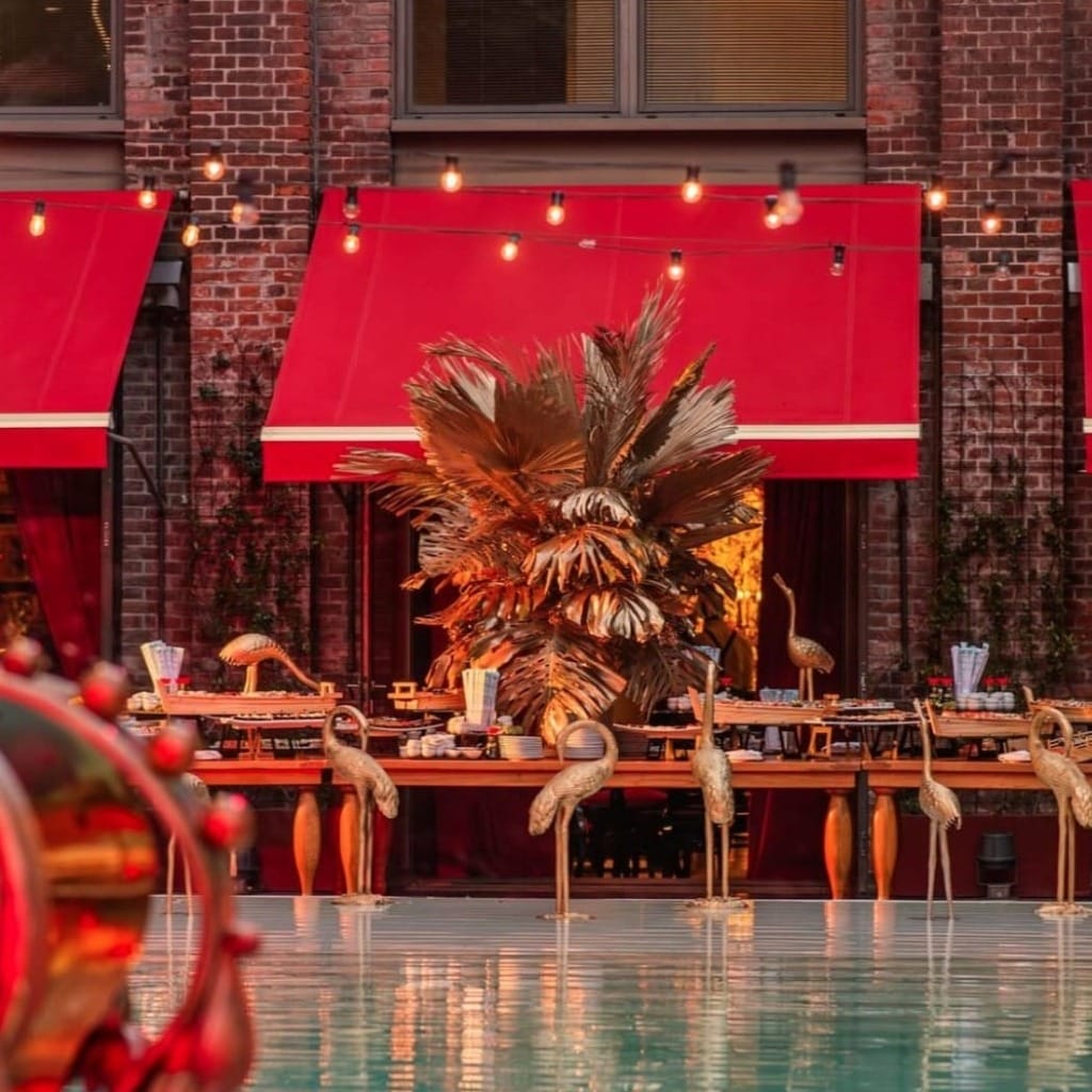Faena Hotel Buenos Aires'in havuz kenarında, altın rengi turna heykelleri, büyük yapraklı süslemeler ve kırmızı tente detaylarıyla zenginleştirilmiş, sanatsal ve dramatik bir atmosfer sunan uzun büfe masaları, Buenos Aires'in tutku dolu enerjisini yansıtıyor.