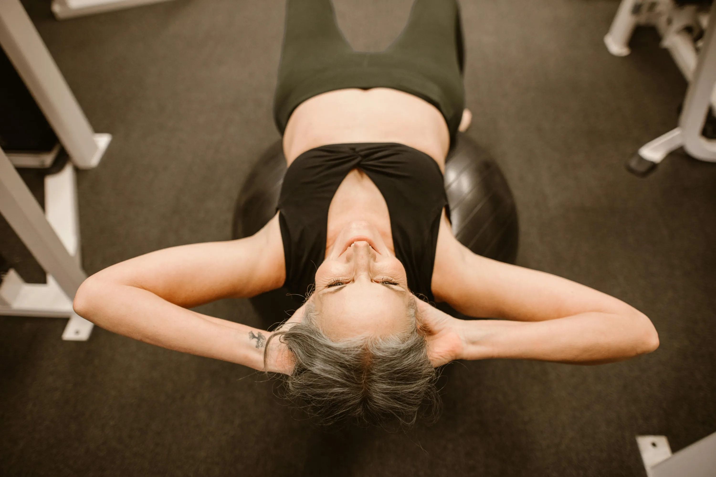 Spor salonunda pilates topu üzerinde mekik çeken olgun kadın; menopoz döneminde aktif yaşam, beden farkındalığı ve sağlıklı yaş alma vurgusu.