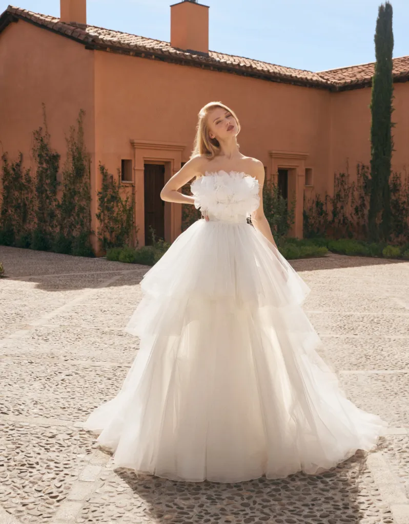 Alberto Palatchi tasarımı, straplez ve üç boyutlu çiçek aplikeleriyle süslenmiş üst kısmı ve kat kat tül etek yapısıyla romantik bir görünüm sunan gelinlik modeli. Açık hava düğünleri için ideal, zarif ve masalsı bir stil.