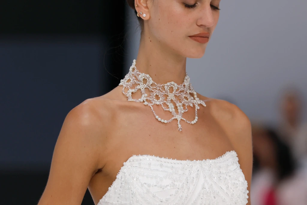 İnci ve kristal taşlarla işlenmiş gösterişli choker kolye takan ve inci detaylı straplez gelinlik giyen modelin yakın çekim görüntüsü.