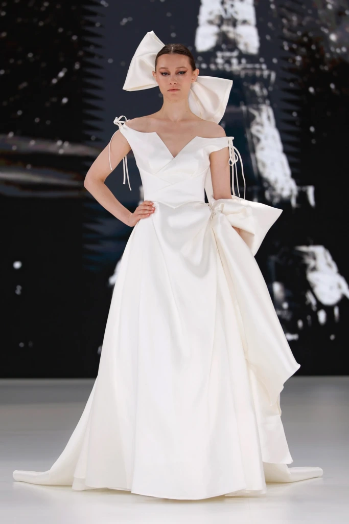 Cymbeline tasarımı, V yakalı, ip askılı ve büyük fiyonk detaylı modern saten gelinlik modeli.