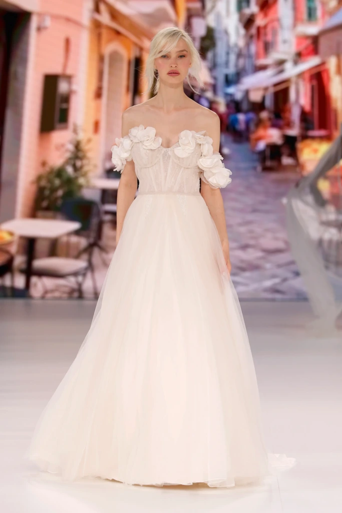 Omuzları çiçek aplikeleriyle süslenmiş, tül etekli, romantik stil bir gelinlik modeli.