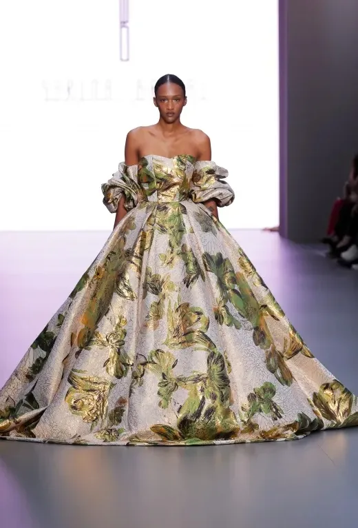 Serina Bridal 2025 İlkbahar koleksiyonundan, altın yeşil floral desenli jakarlı kumaştan tasarlanmış off-shoulder balo tipi gelinlik modeli. Gösterişli silueti ve sanatsal dokusuyla klasik gelinlik kodlarını baştan yazan iddialı bir tercih.