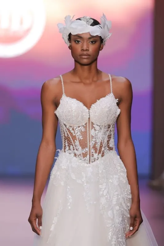 Çiçek aplikeleriyle süslenmiş transparan kollu gelinlik ve dairesel tüy taç detayıyla sıra dışı bridal görünüm