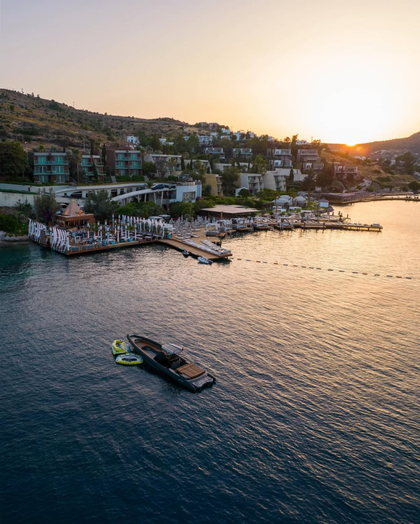 Bodrum'un en iyi eğlence mekanlarından birinin, gün batımının altın rengi ışıkları altında denize uzanan ahşap iskelelerindeki şık restoran ve şezlong alanları ile uzakta demirli lüks bir yatın görüldüğü bu büyüleyici manzara, unutulmaz akşamları çağrıştırıyor.