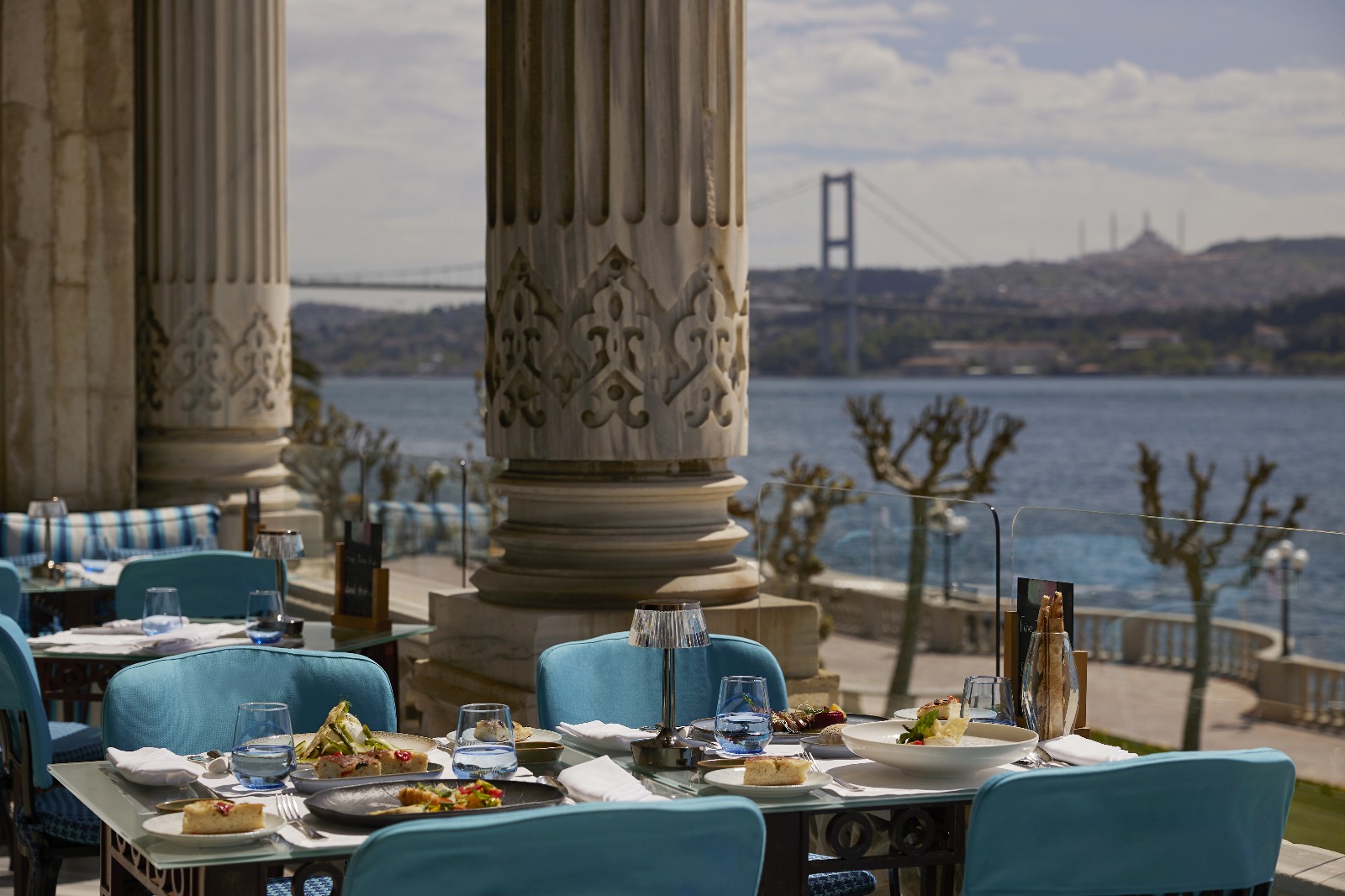 İstanbul'un en iyi teraslı mekanlarından birinde, mermer sütunlarla çevrili şık bir terasta, Boğaz Köprüsü ve tarihi yarımadanın büyüleyici manzarasına nazır masalar lezzetli yemek ve içeceklerle özenle donatılmış, huzurlu bir atmosfer sunuluyor.