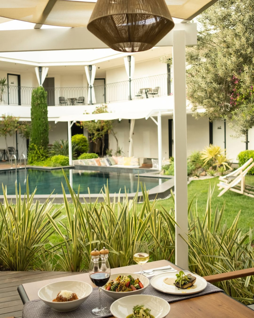 Cunda'nın yemyeşil bahçeleri ve havuzuyla çevrili, şık bir otel veya restoranda, parmesanlı makarna, taze salata ve özenle hazırlanmış ana yemeklerin eşlik ettiği kırmızı ve beyaz şaraplarla dolu masada, adanın zarif ve huzurlu atmosferini yansıtan dingin bir yeme içme deneyimi.