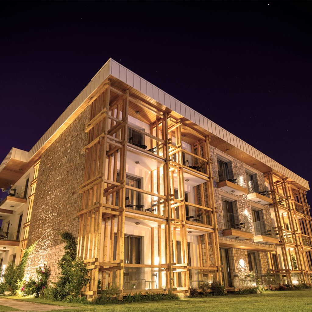 Cunda'nın özgün karakterini yansıtan, taş ve ahşap detaylarla zenginleştirilmiş modern mimarili bir butik otel, gece ışıklandırmalarıyla adanın huzurlu atmosferine zarif bir katkı sunarak misafirlerini eşsiz bir konaklama deneyimine çağırıyor.