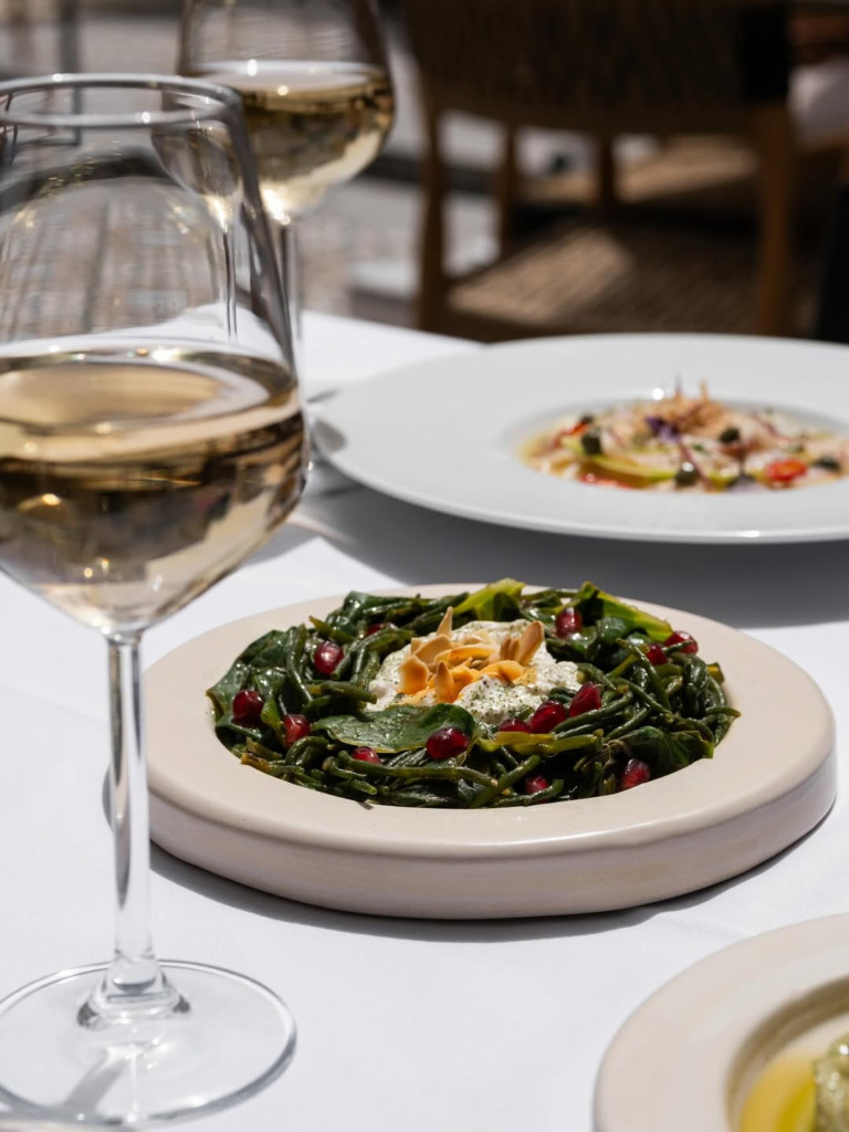 Çeşme/Alaçatı'nın en romantik restoranlarından birinde, beyaz örtülü bir masada duran iki kadeh beyaz şarap ve nar taneleri ile badem dilimleri ile süslenmiş taze yeşil otlar, Ege lezzetlerini yansıtan zarif ve şık bir yemek deneyimini gözler önüne seriyor.