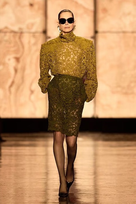 Altın sarısı yüksek yakalı dantel bluz ve uyumlu etekle yürüyen model, couture dokularla modern sofistike bir görünüm sunuyor.