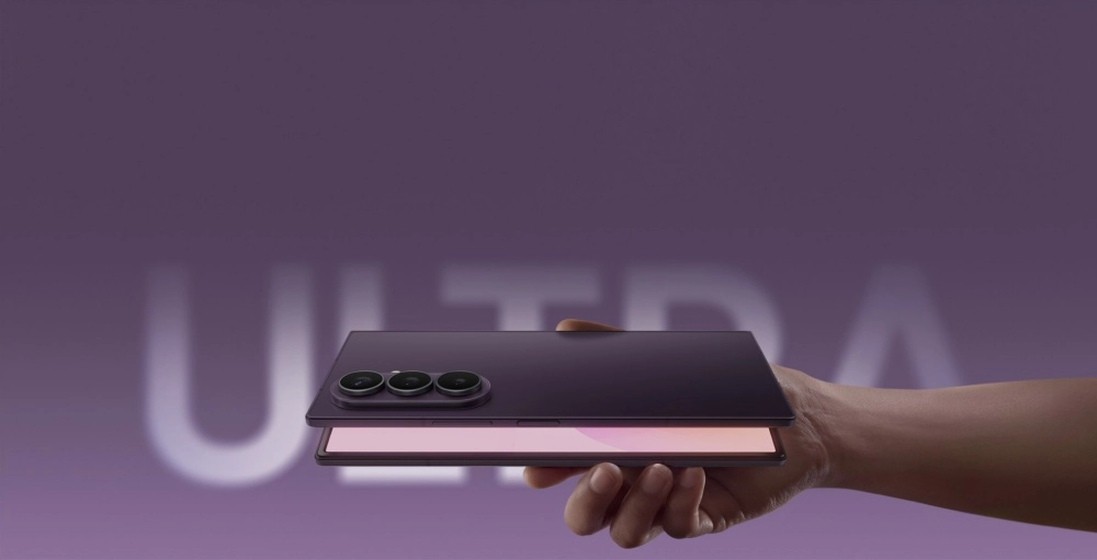 Koyu mor renkli, arka kamerasında üç lens bulunan bir Samsung Galaxy Z Fold 8 Ultra katlanabilir telefon, bir el tarafından hafifçe aralanmış biçimde tutuluyor; telefonun iç ekranı hafif pembe bir ışıkla parlıyor ve mor arka planda büyük, bulanık bir ULTRA yazısı görülüyor.