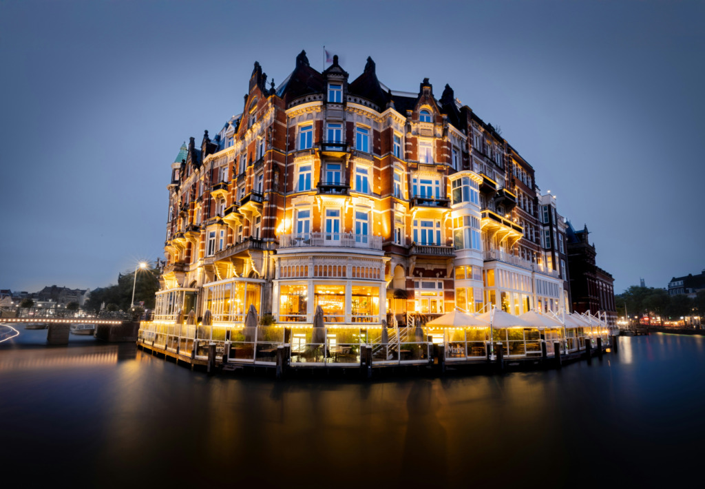 Amsterdam'ın simgelerinden olan, Amstel Nehri kıyısındaki zarif tarihi bina, akşamüstü maviliğinde tüm pencerelerinden ve geniş terasından yayılan sıcak ışıklarıyla kanalların yüzeyinde büyüleyici yansımalar oluşturarak şehrin eşsiz atmosferini vurguluyor.