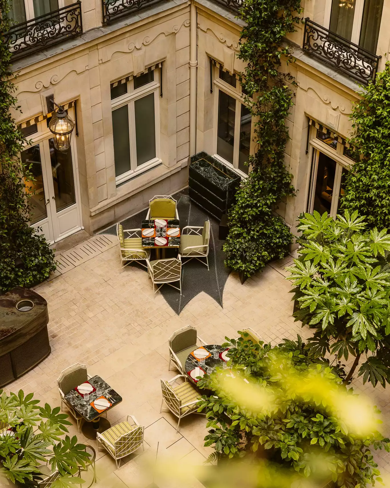 Hotel de Crillon'un, yemyeşil sarmaşıklarla süslü taş binalarla çevrili iç avlusunda, zarif masalar ve konforlu sandalyeler öğle yemeği veya akşam yemeği için şık bir ortam sunarken, huzurlu ve lüks bir dinlenme alanı oluşturuyor.