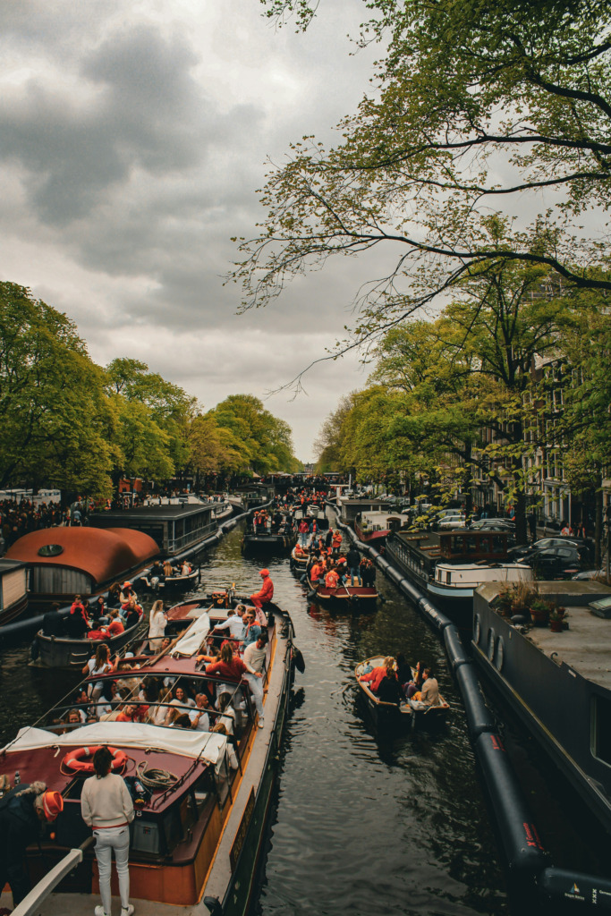 Amsterdam'ın hareketli kanallarında, King's Day kutlamaları sırasında turuncu giysiler içindeki kalabalıklar teknelerle gezintiye çıkmış, ağaçlarla çevrili tarihi binaların önünden geçerek şehrin neşeli ve enerjik atmosferini yansıtıyor.