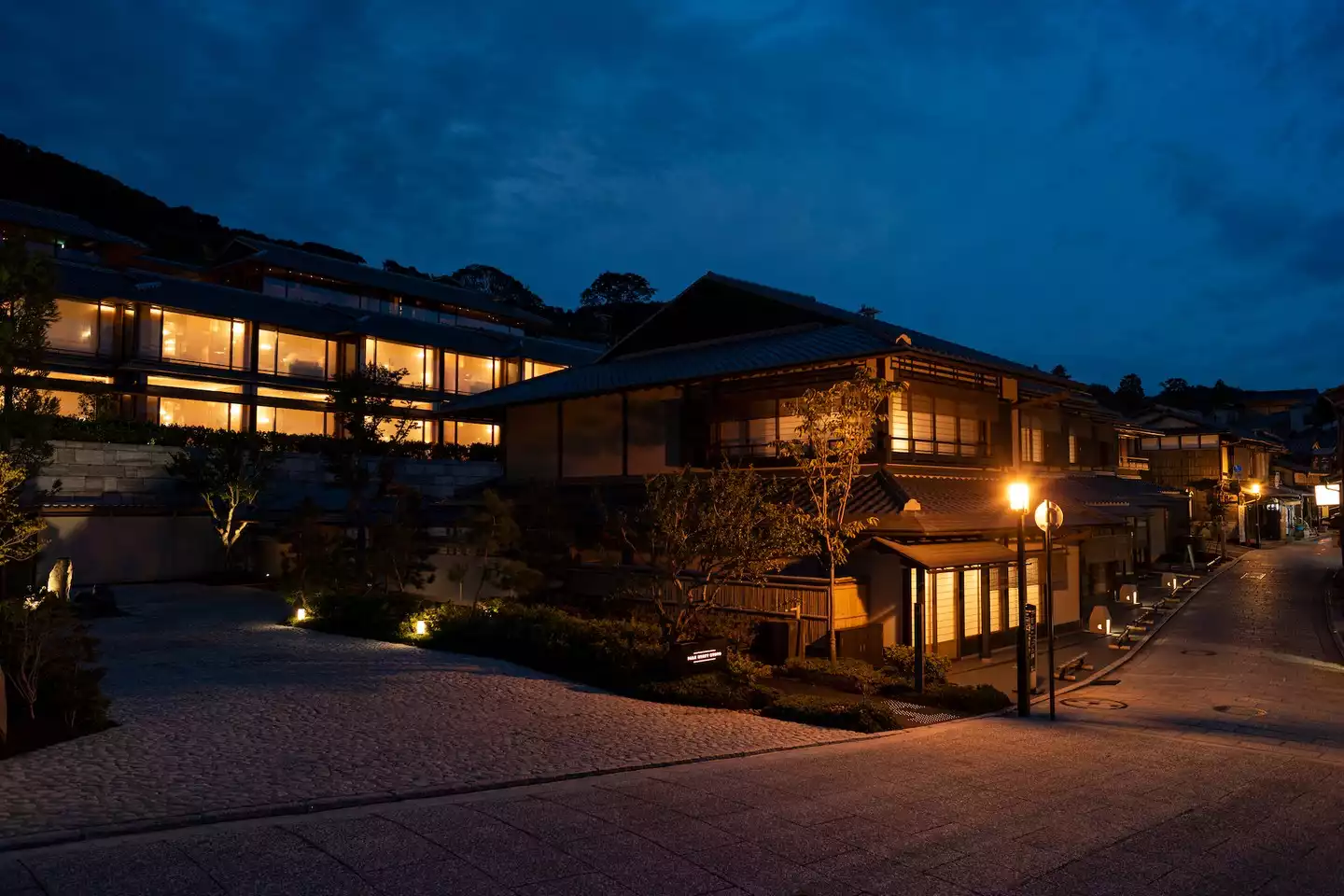 Geleneksel Japon mimarisine sahip Park Hyatt Kyoto otelinin ışıl ışıl pencereleri ve loş sokak lambalarıyla aydınlanan taş döşeli bir Kyoto sokağının alacakaranlıkta çekilmiş büyüleyici bir görüntüsü, çevredeki sakin atmosferi vurguluyor.