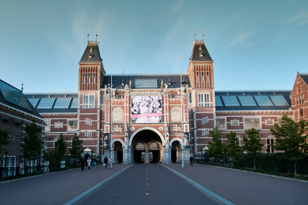 Hollanda'nın sanat ve tarih açısından önde gelen Rijksmuseum müzesi binası, iki yüksek kulesi, kırmızı tuğla ve detaylı mimarisiyle, önündeki geniş yolda yürüyen az sayıda kişinin varlığıyla Amsterdam'ın kültürel yüzünü yansıtıyor.
