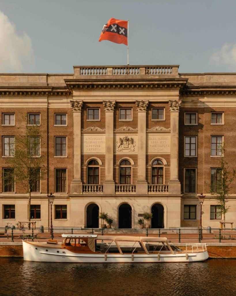 Amsterdam'ın tarihi kanallarından birinde, zarif bir kanal turu teknesinin önünde yükselen, şehrin sembolik bayrağının dalgalandığı, klasik mimariye sahip eski bir adliye binası olan Rosewood otelinin büyüleyici dış cephesi, Amsterdam Seyahat Rehberi'nin ruhunu yansıtıyor.