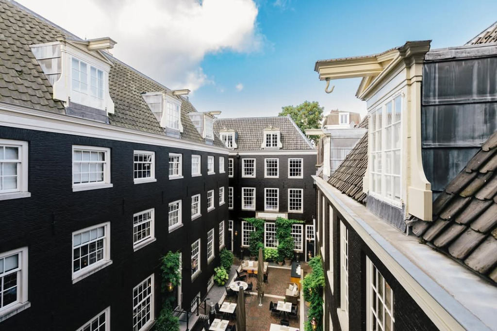 Amsterdam'ın Kanalların ve Sanatın Büyülü Şehri başlığına uygun olarak, Keizersgracht üzerindeki The Dylan Hotel'in, koyu renkli tarihi mimarisi, beyaz pencereleri ve şemsiyeli masalarla dolu, zarif yeşillikler içindeki avlusu.