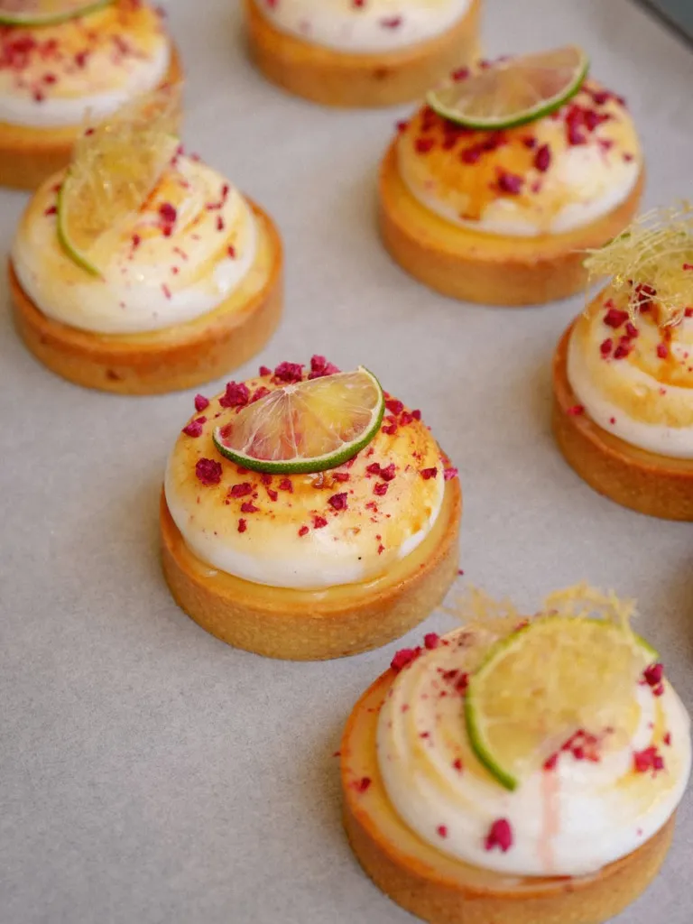 Açık renk bir zeminde düzensizce dizilmiş, altın rengi tart tabanları üzerinde bembeyaz meringue veya krema, taze misket limonu dilimleri, pembe ahududu kırıntıları ve incecik karamel iplikçikleriyle süslenmiş çok sayıda lezzetli tatlı, Lulus Pastane Sapanca'nın özenle hazırladığı el yapımı ürünlerini sergiliyor.
