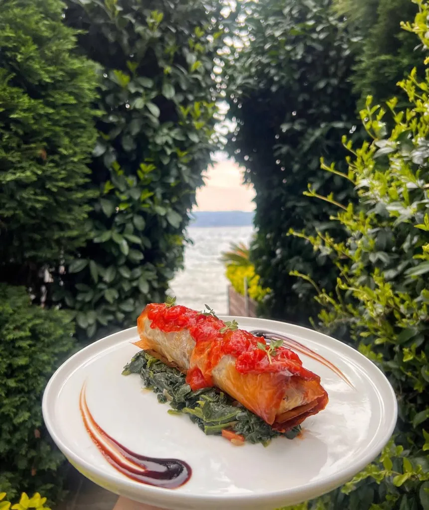 Yeşil bitki örtüsünün çevrelediği, Sapanca Gölü'nün huzur veren manzarasına nazır Sasa Restoran'da, beyaz tabakta servis edilen, altın rengi çıtır yufkadan yapılmış, üzerinde parlak kırmızı domates sosu ve taze kekik bulunan, ıspanak yatağında sunulan zarif bir yemek tabağı.