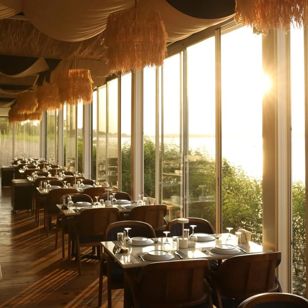 Sapanca Gölü kenarındaki Voda restoranının geniş cam pencerelerinden yansıyan gün batımı ışığıyla aydınlanan, özenle hazırlanmış masaları ve hasır avizeleriyle sıcak bir atmosfere sahip yemek salonu.