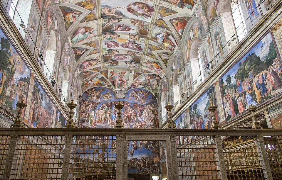 Vatikan'daki Sistine Şapeli'nin, Michelangelo'nun görkemli Yaratılış tavan fresklerini ve sunak duvarındaki Son Yargı'yı içeren muhteşem iç mekanını gösteren bu geniş açılı görüntüde, alt kısımda süslü bir ızgara ve şamdanlar belirginleşiyor.