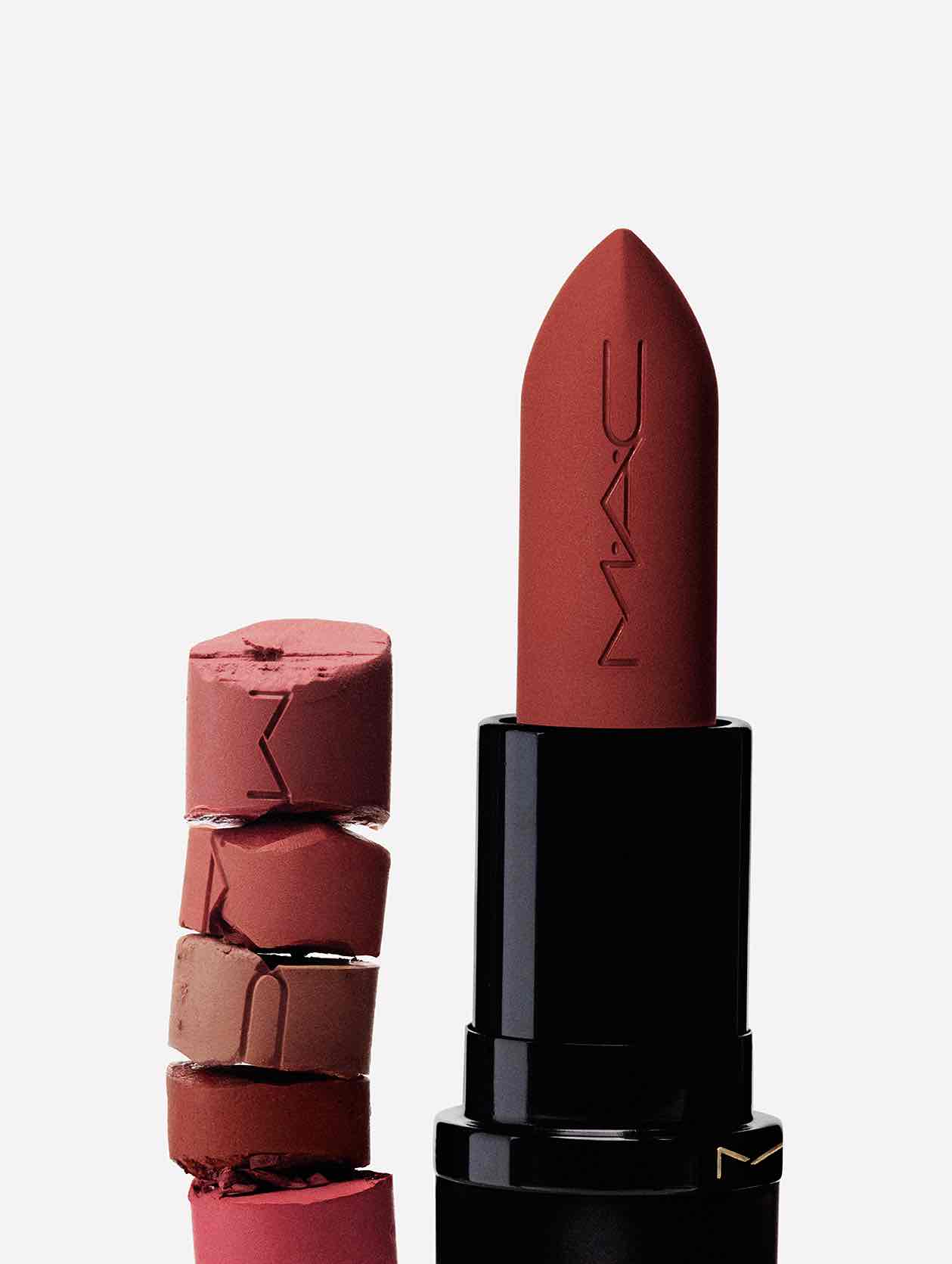 MAC Hazy Matte koleksiyonunu temsil eden pas kırmızısı ruj, yanında çeşitli nude ve pembe tonlarda kırılmış parçalarla birlikte mat dokusunu ve zengin renk yelpazesini vurguluyor.
