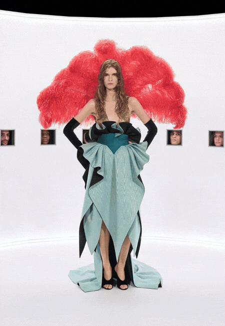 Haute couture defilesinde podyumda sunulan, siyah detaylarla vurgulanan heykelsi formda turkuaz couture elbise ve dramatik kırmızı arka plan yerleştirmesi.