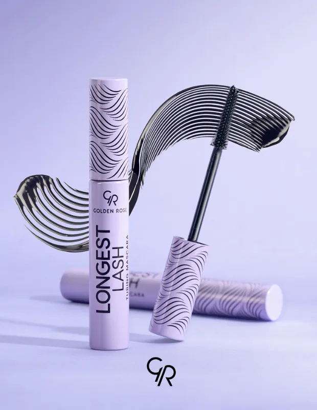 Açık mor bir arka plan üzerinde, Golden Rose markasının Longest Lash Tubing Mascara yazılı lila renkli tüpü dik bir şekilde konumlanmış; yanındaki aplikatör fırçası yoğun siyah maskara ürünüyle bükülerek yukarı doğru uzanıyor ve tüplerin kapaklarındaki dalgalı desenleri yansıtan estetik bir leke oluştururken, arka planda aynı seriden bir maskara tüpü yatay olarak duruyor.