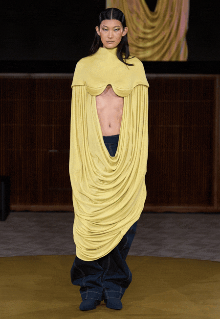 London College of Fashion 2026 Sonbahar-Kış koleksiyonunda akışkan drapeli sarı üst tasarım, açık gövde detayı ve minimal formuyla modern, deneysel ve heykelsi siluet.