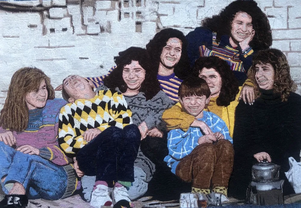 Bu serbest el makine nakışı eserinde, yaşları farklı sekiz kişi neşeyle gülümseyerek, kimisi kahkahalar atarak ve birbirlerine sarılarak samimi bir anı paylaşırken, canlı renkli kazakları ve dokulu arka plan detaylarıyla sıcak bir aile fotoğrafı havası yansıtıyor.