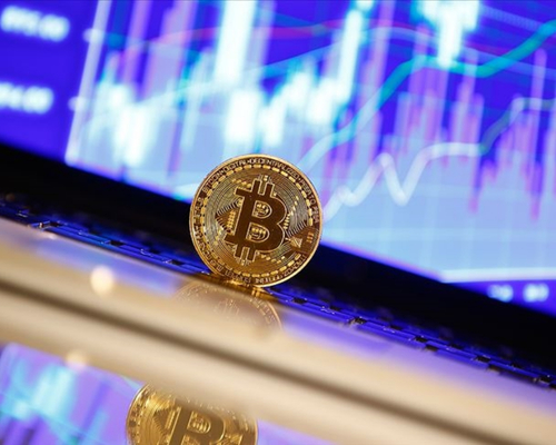 Parlak bir yüzey üzerinde dik duran altın renkli Bitcoin madeni parası, arka planda dijital finansal piyasaların dalgalanmalarını gösteren mavi ve mor tonlardaki grafiklerle birleşerek kripto para dünyasının dinamiklerini yansıtıyor.