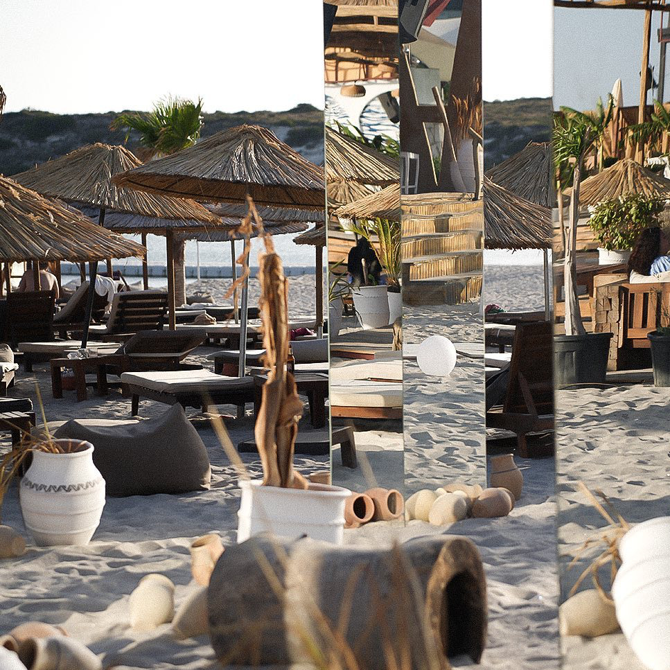 Sakin kumsalda hasır şemsiyeler, konforlu şezlonglar ve dekoratif seramik saksılarla dolu Alaçatı’daki Kali Beach’in parçalı, sanatsal bir görüntüsü, Çeşme beach club'larının huzurlu ve zarif ambiyansını vurguluyor.
